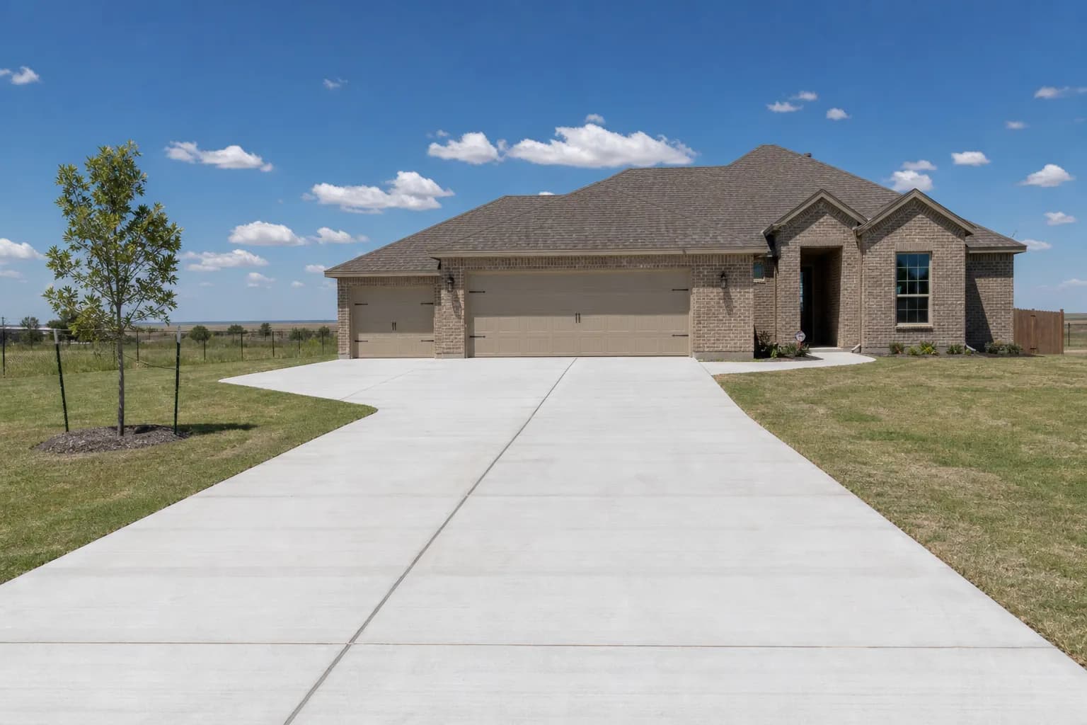Wide new two-car concrete driveway with saw-cut joints in front of a tan brick home with a three-car garage